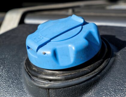 A container of diesel exhaust fluid next to a gasoline engine, illustrating potential risks and safe practices.