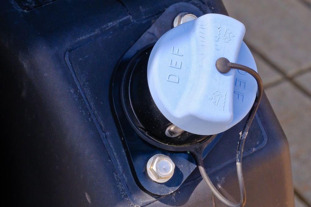 A container of diesel exhaust fluid next to a gasoline engine, illustrating potential risks and safe practices.