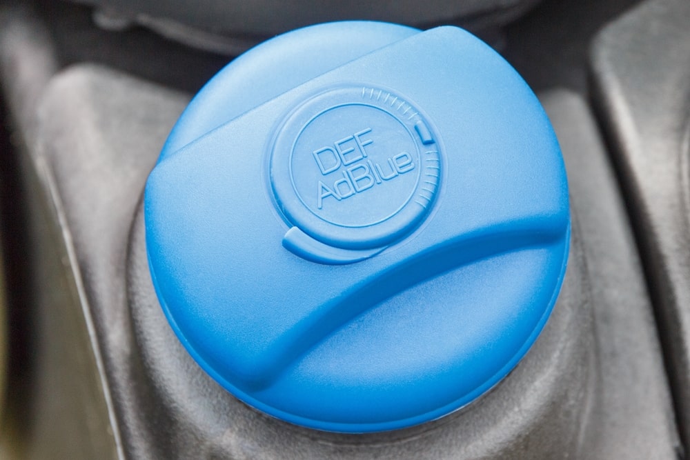 A container of Diesel Exhaust Fluid being poured into a truck’s DEF tank.