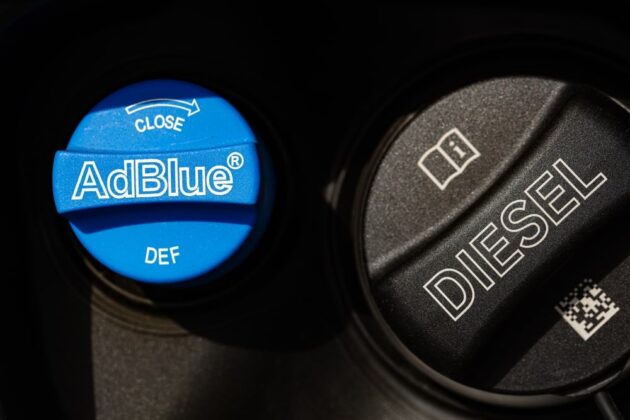 A container of Diesel Exhaust Fluid being poured into a truck’s DEF tank.