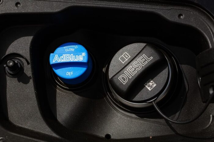 Technician refilling a Sprinter van’s diesel exhaust fluid (DEF) tank at a shop bay.