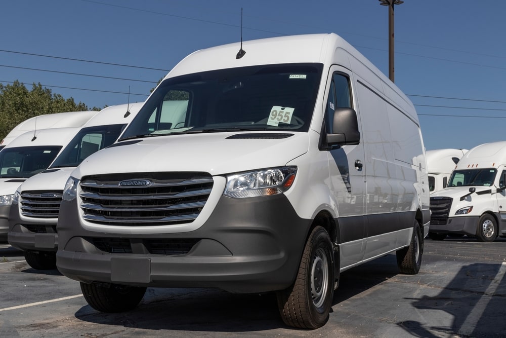 Technician refilling a Sprinter van’s diesel exhaust fluid (DEF) tank at a shop bay.