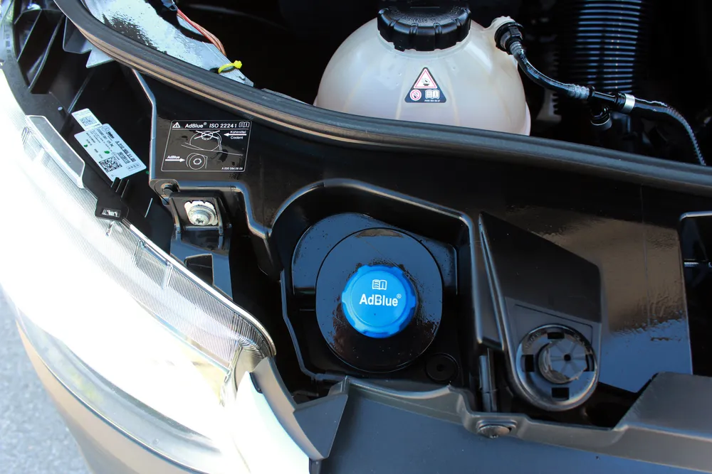 Diesel vehicle dashboard showing AdBlue warning with DEF refill container nearby