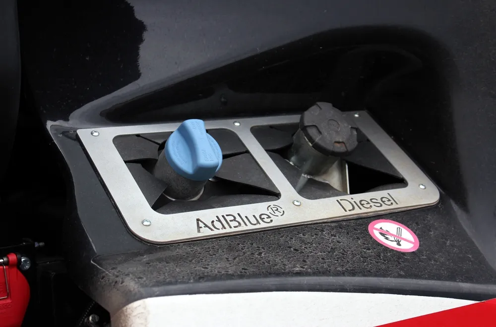 Diesel vehicle dashboard showing AdBlue warning with DEF refill container nearby