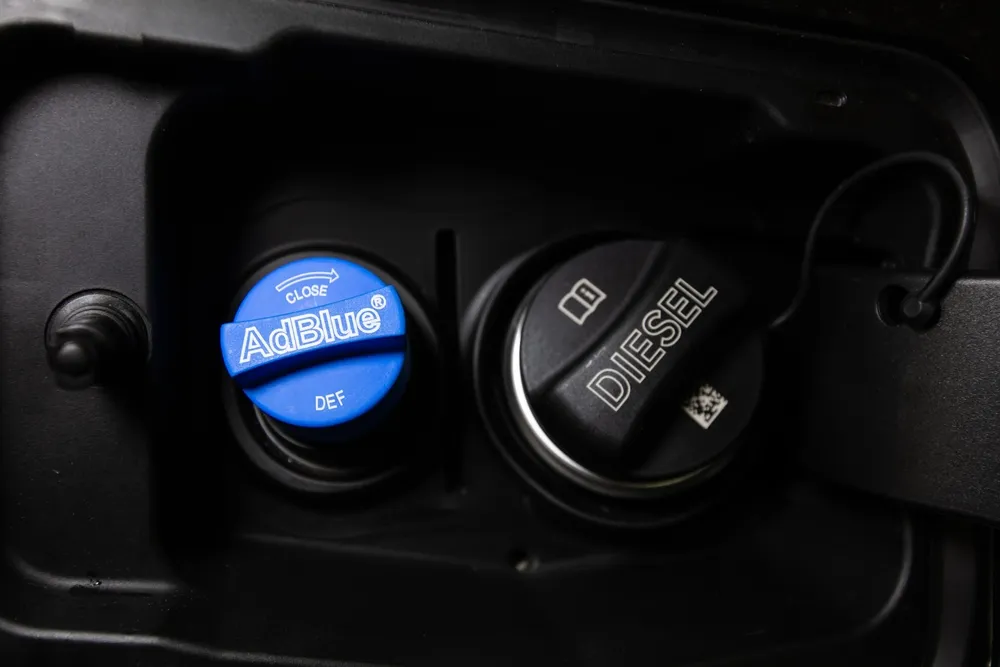 Diesel vehicle being refilled with AdBlue diesel exhaust fluid near a fuel pump